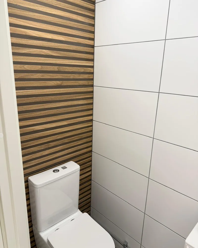 Toalettrum renoverat av BHB Bygg AB med träribbor på väggen och stort vitt kakel.